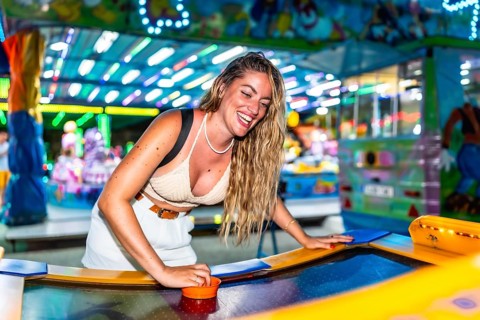 Young woman enjoying a game of air hockey at a brightly lit amusement park, laughing and having a