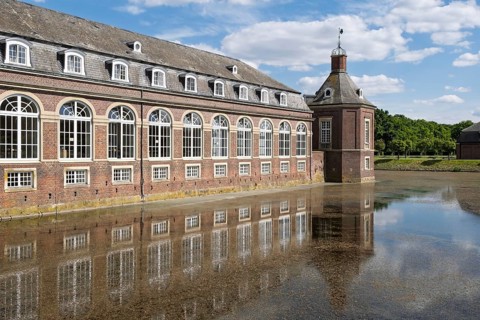 Historic brick building reflected in calm water under a blue sky and clouds, Nordkirchen Castle,