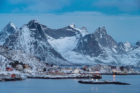 Fishermen's Village in front of snowy mountain range at the coastline in winter, Lofoten, Norway