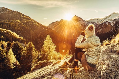 Woman sitting thoughtfully at a feslen at autumn atmosphere during sunset in the Swiss Alps in the