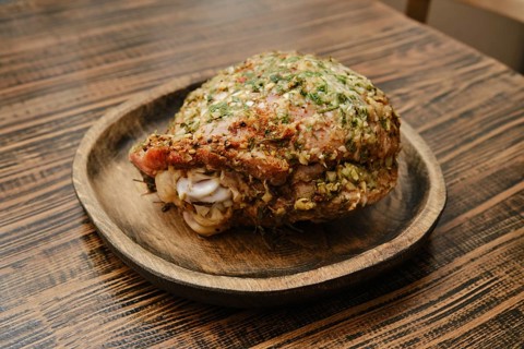 A roasted turkey thigh on a round wooden plate. The thigh is seasoned with fresh herbs, showcasing