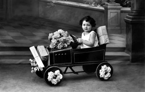 Child in toy car, 1920s, A child drives a toy car, decorated with flowers, in a nostalgic black and