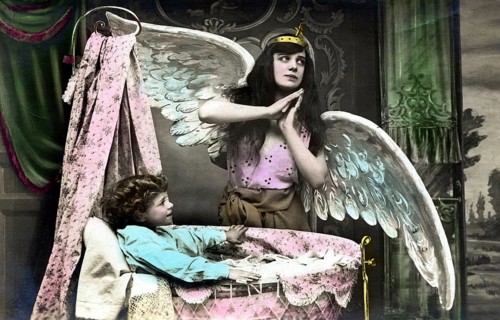 Angel with infant, 1920s, child lying in a cradle while a girl poses as an angel, historical photo