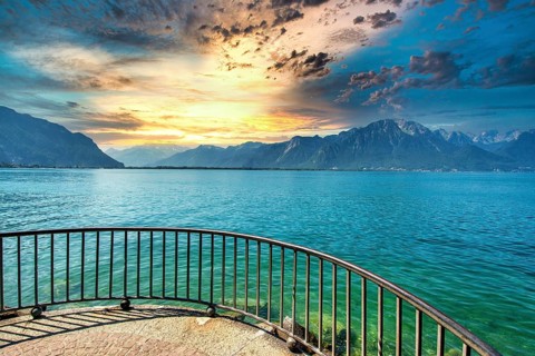 Golden light reflects on the calm waters of Lake Leman as clouds gather over the mountains in