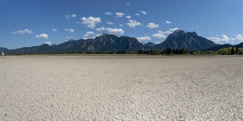 Cracked, dried out ground, waterless Forggensee in spring, behind it Tegelberg massif and Säuling,