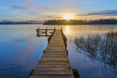 Wooden footbridge leading into the water at sunrise over a calm lake, Lake Mahinapua, Ruatapu,