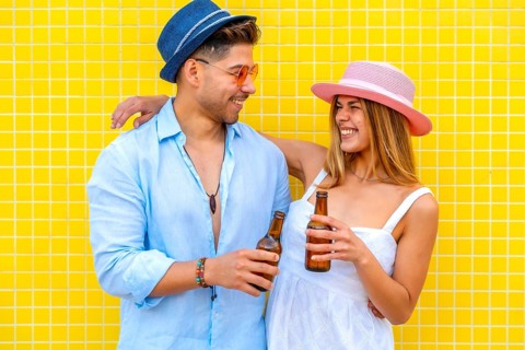 Young tourists drinking bottled beer, wearing summer clothes and hats, smiling and having fun on a