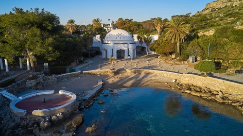 Drone shot, morning light, building with dome on a small beach with turquoise water, surrounded by