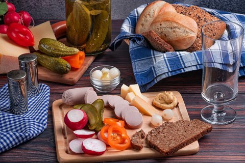 Rustic snack with sausage, cheese, vegetables, mustard and bread on a laid table