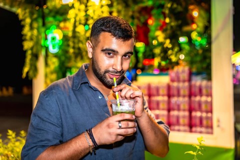 Young man sips a mojito through a straw at a vibrant night market, enjoying the festive atmosphere