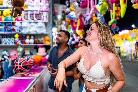 Happy friends playing at a throwing game stall trying to win plush toys at amusement park at night
