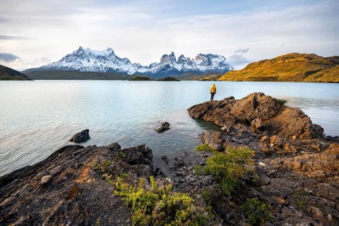 Young man on the shore of the blue lake Lago Pehoe in the evening light, Cuernos del Paine mountain