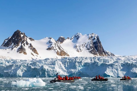 Group of Zodiacs in front of glacier and mountain range with snow, sea, Fugelfjorden, Spitsbergen,