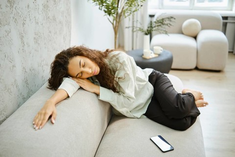 A woman with long curly hair leans against a light-colored couch, appearing relaxed and at ease