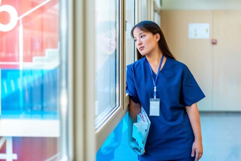 Thoughtful medical professional pausing in hospital hallway, holding patient files and gazing