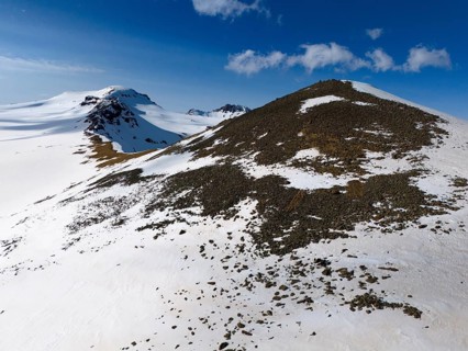 Near a snow-covered hilltop with rocks on the descent under a clear sky, aerial view, Aragaz,