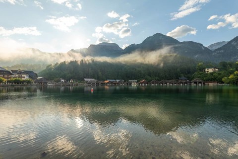 Mystical morning at Königssee in Schönau with boathouses. Sunrise and beautiful wafts of mist over