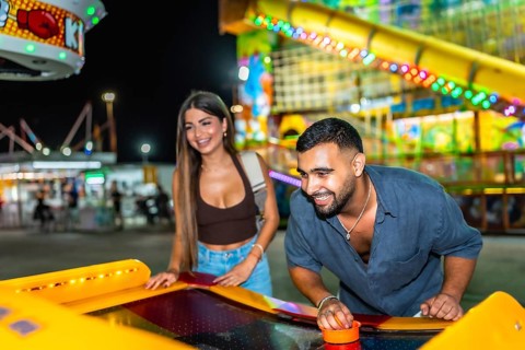 Young man and woman having fun playing air hockey at amusement park at night, enjoying their