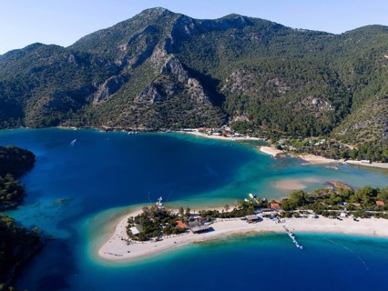 Panoramic picture with coastline and sandbank, surrounded by turquoise water and green hills,