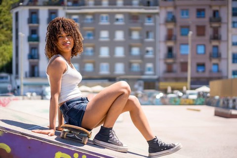 Young woman sitting on her skateboard atop a ramp in an urban skatepark, soaking up the sun on a