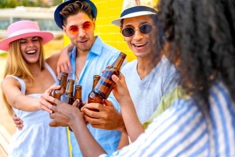Cheerful multi ethnic friends enjoying a summer party, toasting with beer bottles against a vibrant
