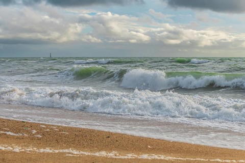 Powerful ocean waves wash over a sandy beach, creating white foam against a backdrop of dramatic