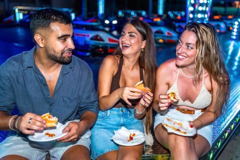 Three friends are enjoying hot dogs together at an amusement park, laughing and having a good time
