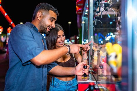 Happy couple enjoying a night out, playing a claw crane game at an amusement park, trying their