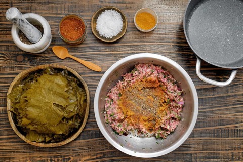 Preparing dolma involves mixing ground meat with spices and herbs on a rustic kitchen table. Fresh
