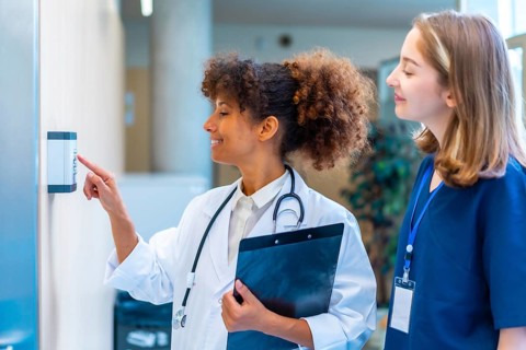 Female doctor entering security pin code on keypad access control, next to a nurse, in a hospital