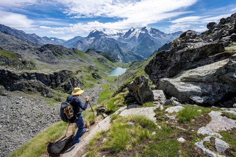 Mountaineer on hiking trail in mountain landscape, descent at Col du Louvie, view of mountain lake