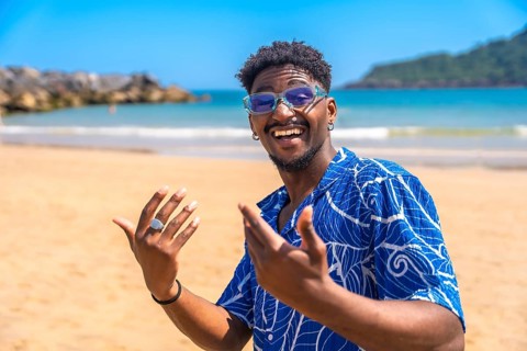 Young man enjoying summer vacation on a tropical beach, smiling widely and gesturing joyfully while