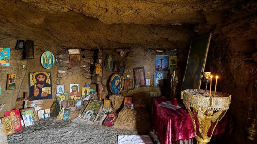 Religious sanctuary in a cave with orthodox icons and burning candles on an altar, chapel, Agios