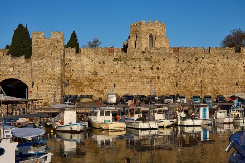 Boats moored in front of an old harbour wall with historic tower, Rhodes Old Town, Rhodes,