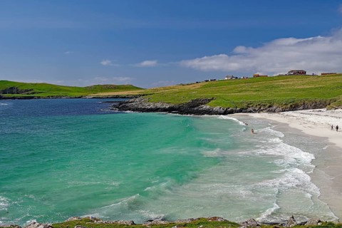 A picturesque beach with turquoise waters and gentle waves under a blue sky, surrounded by green