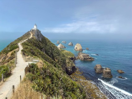 Nugget Point Lighthouse with Nugget Rocks in front of a blue sky, South Island, New Zealand,