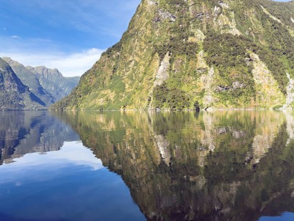 Mountains with reflections in the water against a blue sky in Doubtful Sound, South Island, New