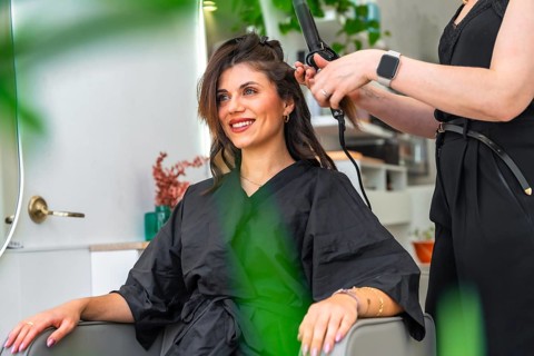 Hairdresser styling hair of a smiling client with a curling iron in a chic, modern beauty salon,