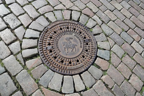 Round manhole cover with city coat of arms and inscription, state capital, paving stones, floor,
