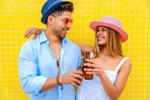 Young stylish tourists toasting with beer bottles, enjoying summer vacation together against a