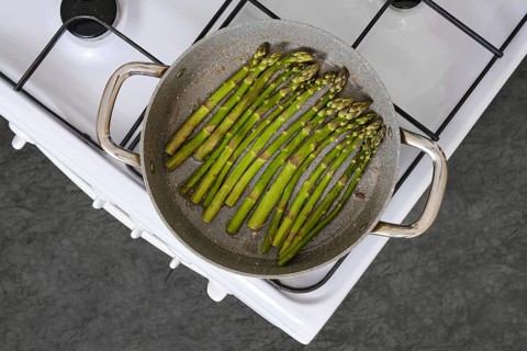 Fresh green asparagus is being cooked in a pan on a gas stove in the kitchen. The texture of the