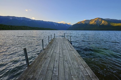 Wooden walkway stretches across the lake with mountains at sunrise, summer, Lake Rotoiti, Saint