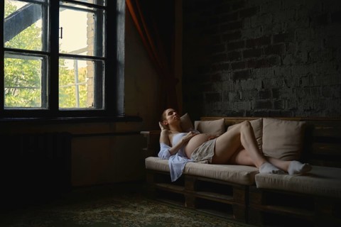 A pregnant woman lounges comfortably on a cozy couch in her home. The warm sunlight filters through
