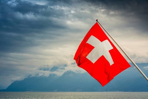 View of the Swiss flag waving over Lake Geneva with mountains and clouds in Switzerland during a