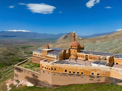 Historic fortress in Turkey, surrounded by green landscape and mountains, under a blue sky, aerial