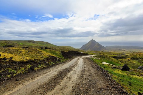 Gravel track through barren moss-covered volcanic landscape, cone-shaped mountain Stapafell, rain