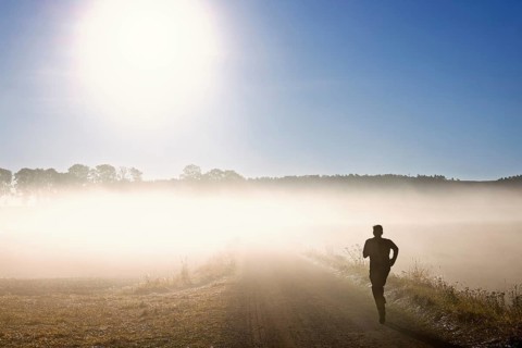Man training running on a gravel road in the morning fog in a rural landscape with the sun shining