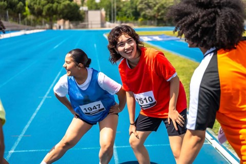 Runners stretching their legs on a vibrant blue track, recovering after a race, embodying teamwork