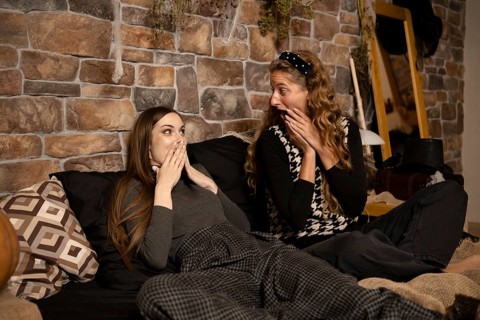 Two friends express surprise and excitement while lounging on a comfortable bed in a warmly