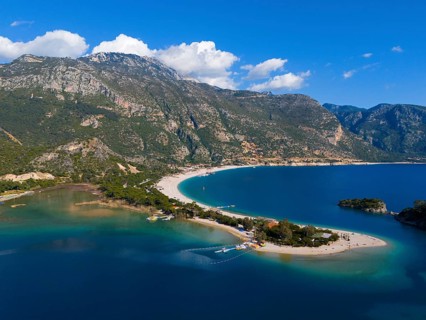 View of a beach with a peninsula surrounded by mountains and blue sea under a clear sky with